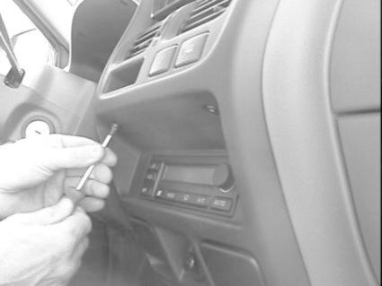 En hand håller i en skruvmejsel nära bilens stereoenhet.