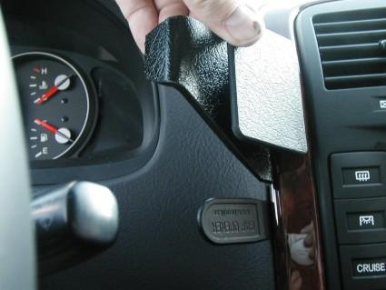 En hand som håller i en svart plastdel på en bilinteriör.