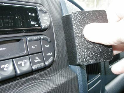 En hand håller en vinklad svart kloss nära en bilradio.