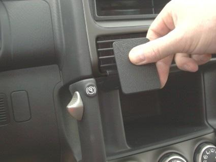 En hand som håller en platt bit, vid en luftventil i en bil.