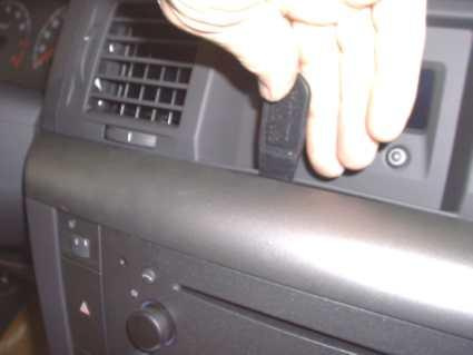 Hand som håller en svart knapp på instrumentbrädan i Opel Signum/Vectra.