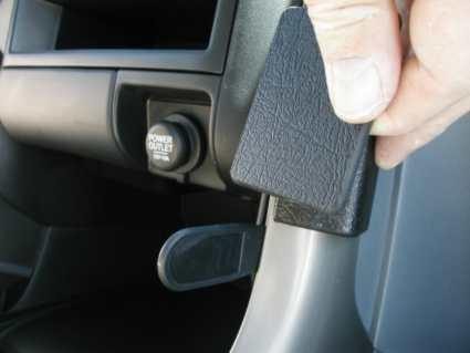 En hand som håller i en plastdel inuti en bil, med en strömbrytare synlig.