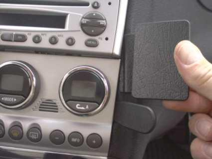 En hand håller en svart platta vid bilens instrumentpanel och kontroller.