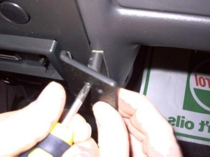 En person använder en skruvmejsel för att montera något i en bils interiör.