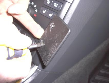 En person skruvar bort en svart platta i en bil, troligtvis en Volvo XC90.