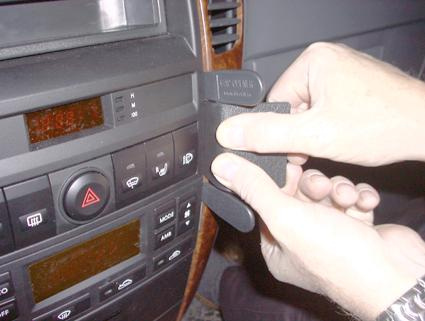 Händer som installerar en svart detalj i en bil med brun träpanel.