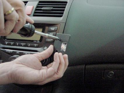 En hand håller en skruvmejsel mot en del av bilens interiör.