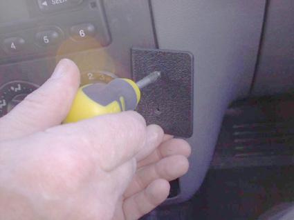 En hand håller en skruvmejsel mot en svart plastdel inuti en bil.