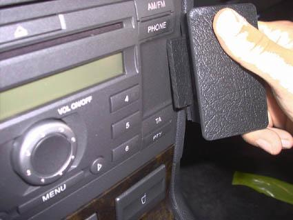 En hand som håller en svart platta nära bilens radio och kontroller.