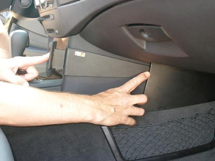 En hand pekar på ett utrymme i bilen, troligtvis en förvaringslåda.