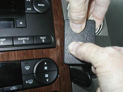 En hand trycker på en svartsidig knapp eller panel i en bilinteriör.