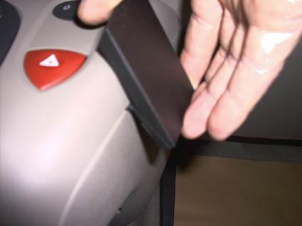 En hand håller en svart del nära bilen, troligen en del av inredningen.