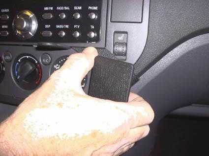 En hand håller en svart enhet nära bilens kontrollpanel.