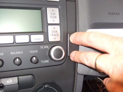 En bild av en bilstereo med knappar och en hand som pekar.