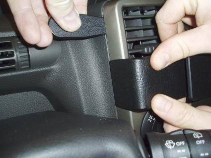 En person fäster ett svart plastmaterial vid en luftventil i bilen.