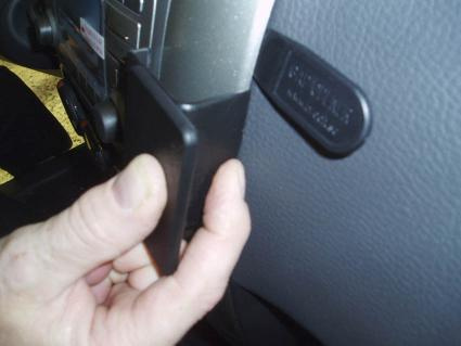 En hand håller i en vinklad svart plastdel, troligen en bilkomponent.