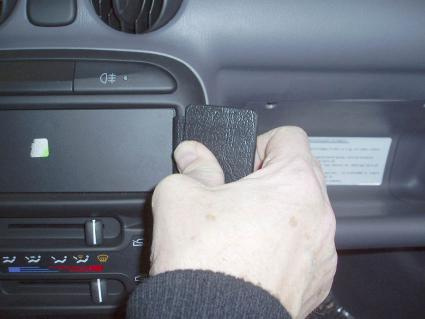 En hand håller en svart del nära bilens instrumentbräda.