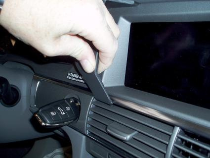 Hand som använder ett verktyg för att justera eller ta bort en del av instrumentpanelen.