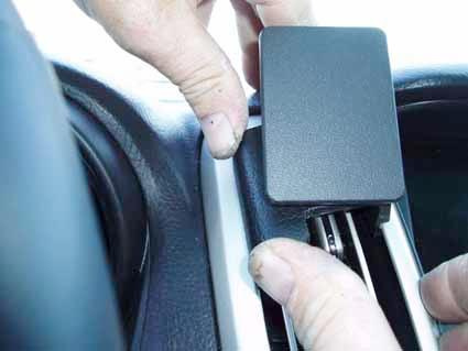 Händer monterar en svart komponent i en bils interiör.