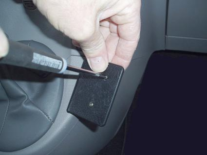 En hand håller en skruvmejsel mot en svart plastdel inuti en bil.