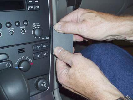 En person installerar eller justerar en del på instrumentpanelen i en Volvo V70.