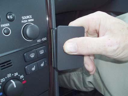 En hand håller en svart panel i en bilinteriör.