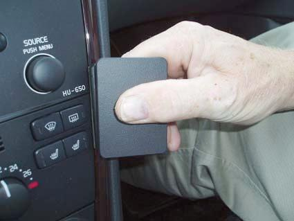 Hand håller i en svart panel, troligen från bilens interiör.