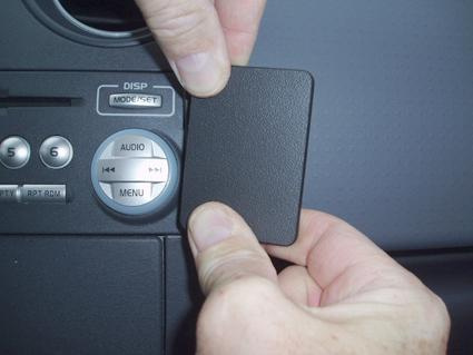 En hand som håller en svart knapp vid en bils kontrollpanel.