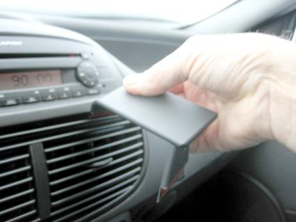 Hålls en vinklad monteringsbygel för Fiat Punto i en hand, nära en bilradio.