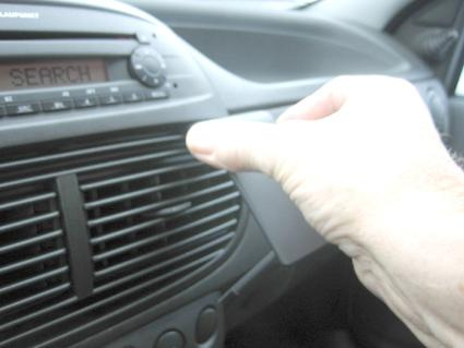 En hand visar en grå monteringsbygel i en bilinteriör.