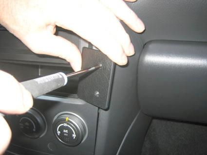 En hand installerar en komponent med en skruvmejsel i en bils inredning.