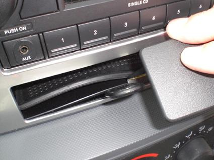 En hand som öppnar en lucka på bilens stereo.