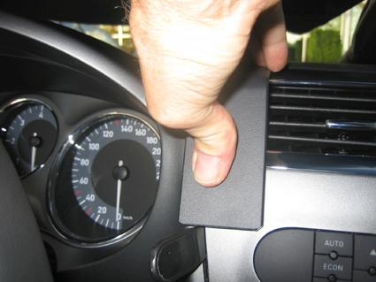 En hand håller en del som delvis täcker bilens instrumentpanel.