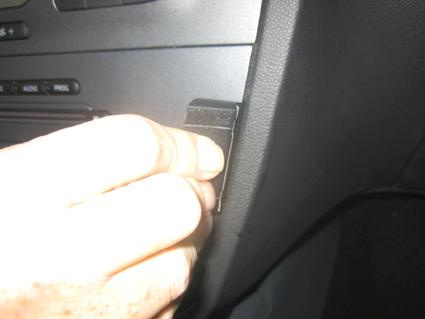 En hand som trycker på en svart knapp i en bilinteriör.