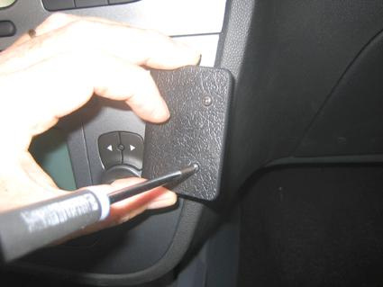 En hand håller i en skruvmejsel mot en svart panel i en bil.