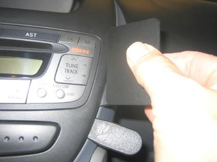 En hand håller en svart platta nära bilens stereo- och kontrollpanel.