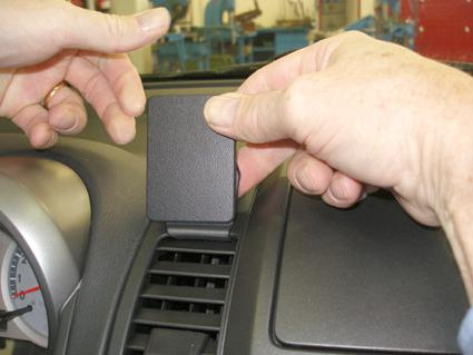 Två händer håller i en svart plastdel som ska monteras på en bils instrumentbräda.