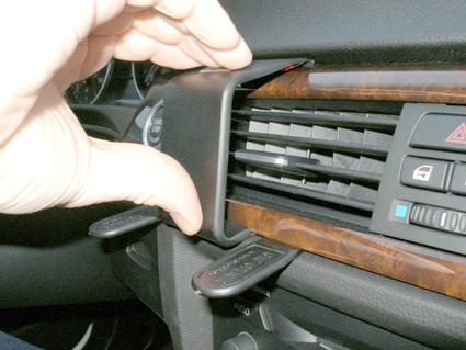 En hand som tar bort en del av träpanelen från en bils luftutblås.