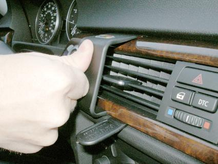 En hand justerar luftventilen på en BMW, med träpanel.