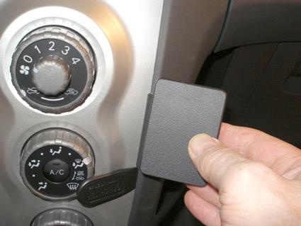 En hand håller i en svart panel framför bilens knappar och reglage.