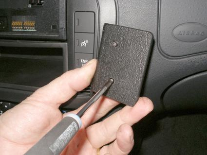 En hand håller i en skruvmejsel mot en plastdel i bilen.