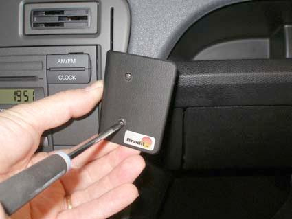 En hand som håller en skruvmejsel mot en enhet i en bil.