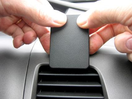 En hand placerar en svart plastdetalj på en bils instrumentpanel.