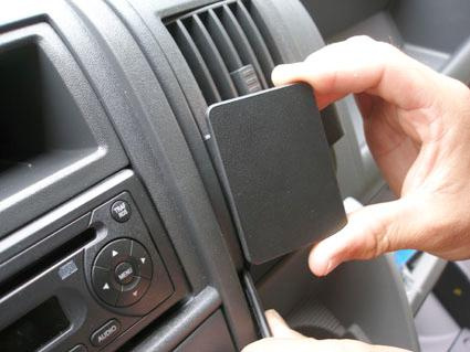 En person installerar en enhet i en bils interiör, nära luftutblåset.