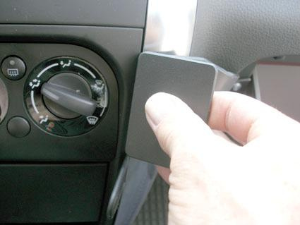 En hand håller i en svart komponent nära bilens kontroller.