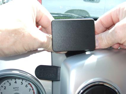 En person håller i en svart rektangulär enhet nära bilens instrumentpanel.