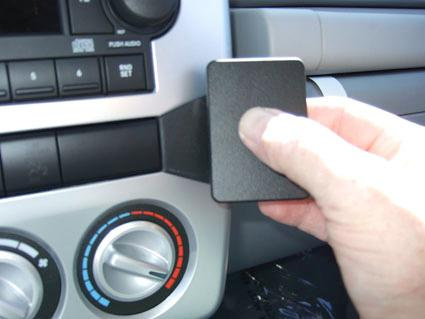 En hand håller en svart plastdel nära en bilkontrollpanel.