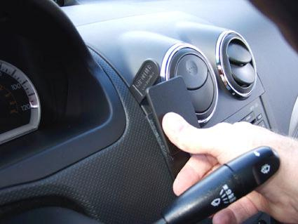 En hand placerar en svart enhet på instrumentpanelen i en Chevrolet Aveo.