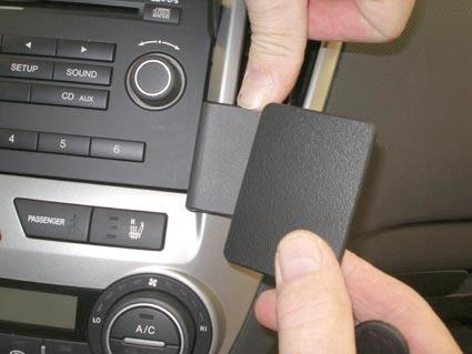 Hand som håller en svart panel i bilen, nära inbyggd ljudkontroll.