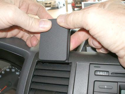 En hand sätter på en svart del på luftventilen i en bil.